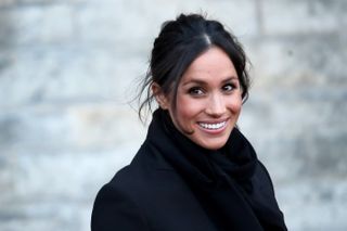 A close up of Meghan, Duchess of Sussex dressed in black and smiling.