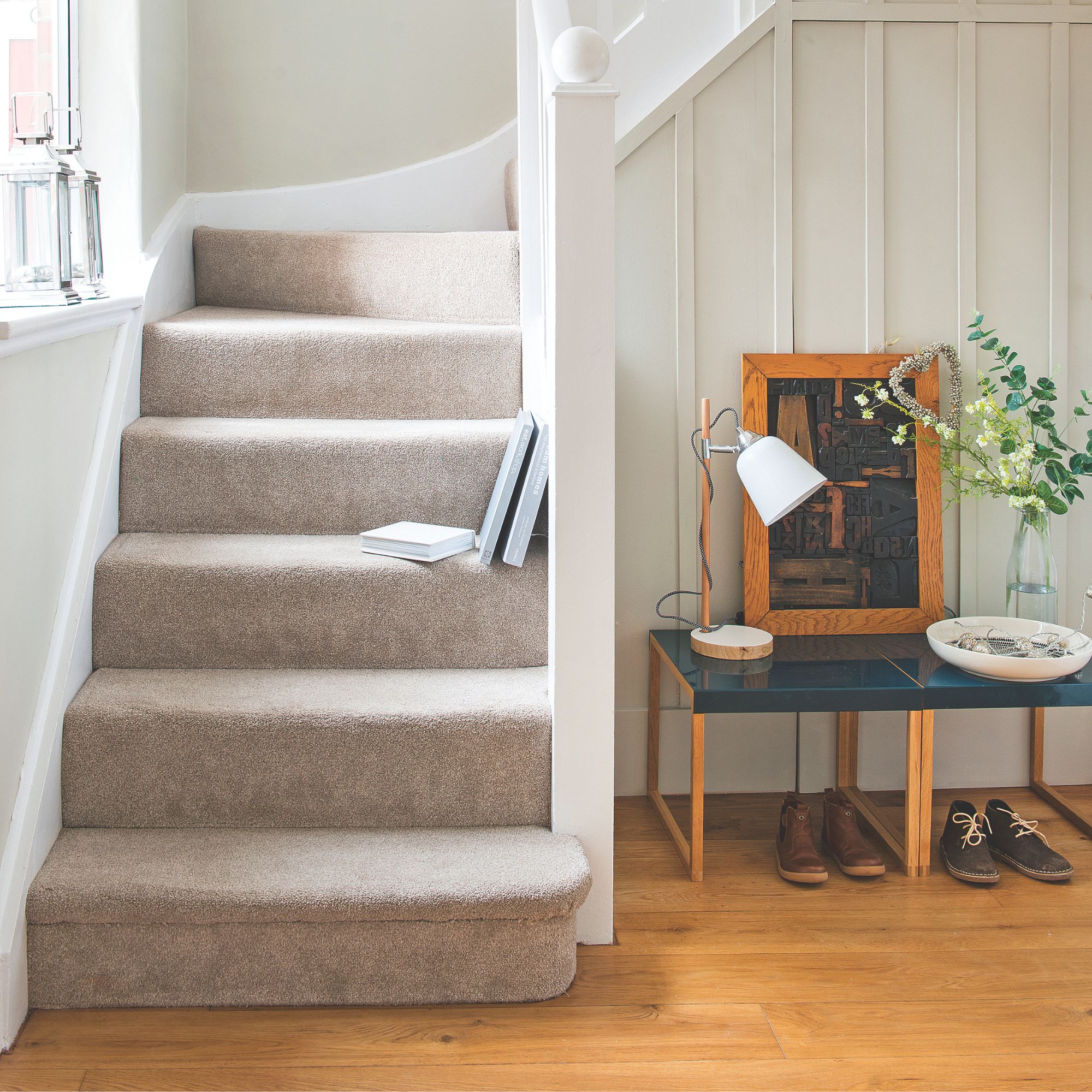 Hallway with wooden floors and carpeted stairs, and a table with shoes underneath beside it