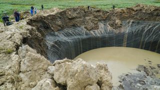 People stand on the edge of the giant Yamal crater, which has almost filled with water since it erupted.