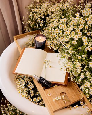 Daisies sprout out of a white bathtub adorned with a candle.