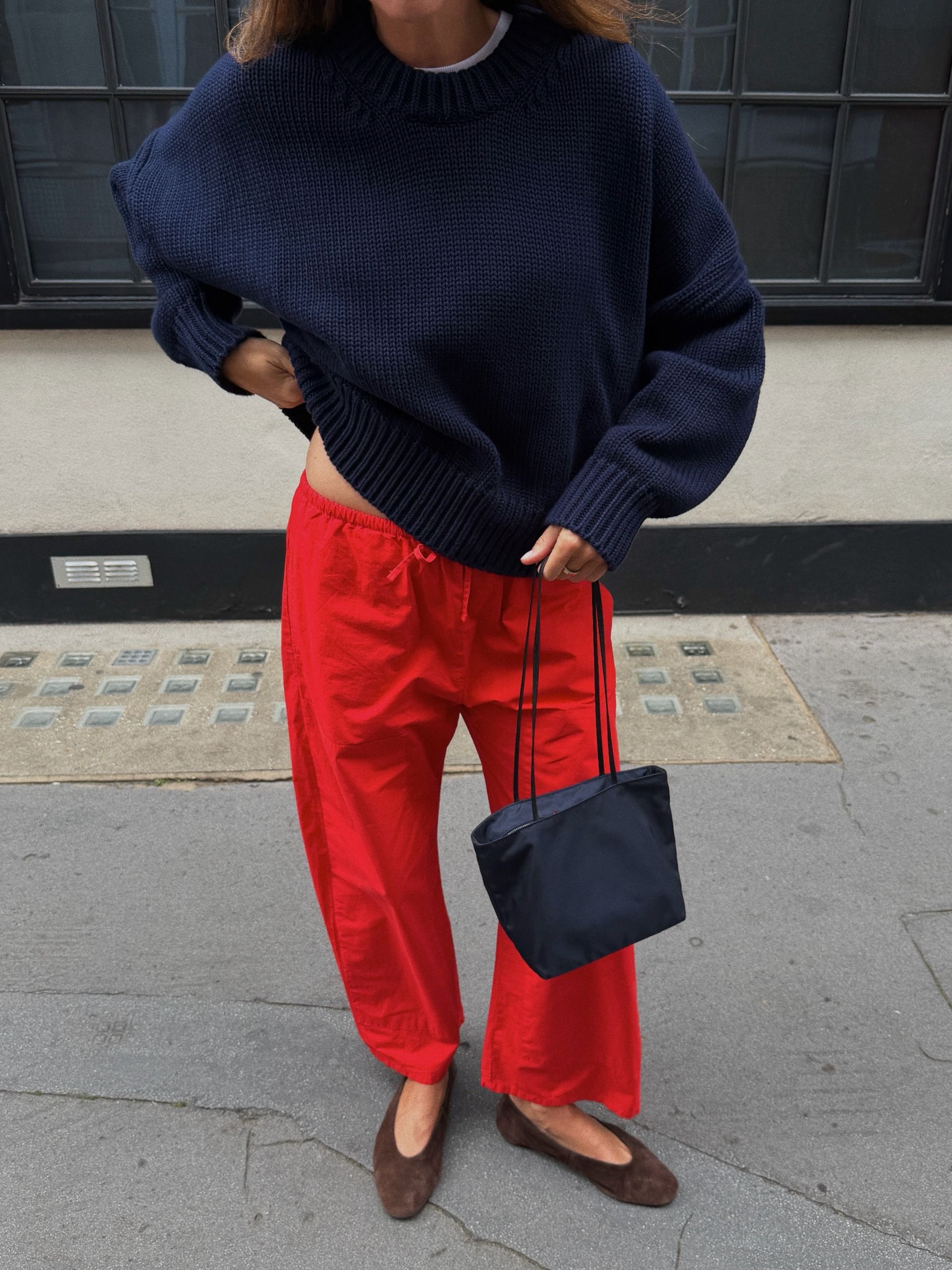 Woman in a navy sweater, red pants, and brown ballet flats