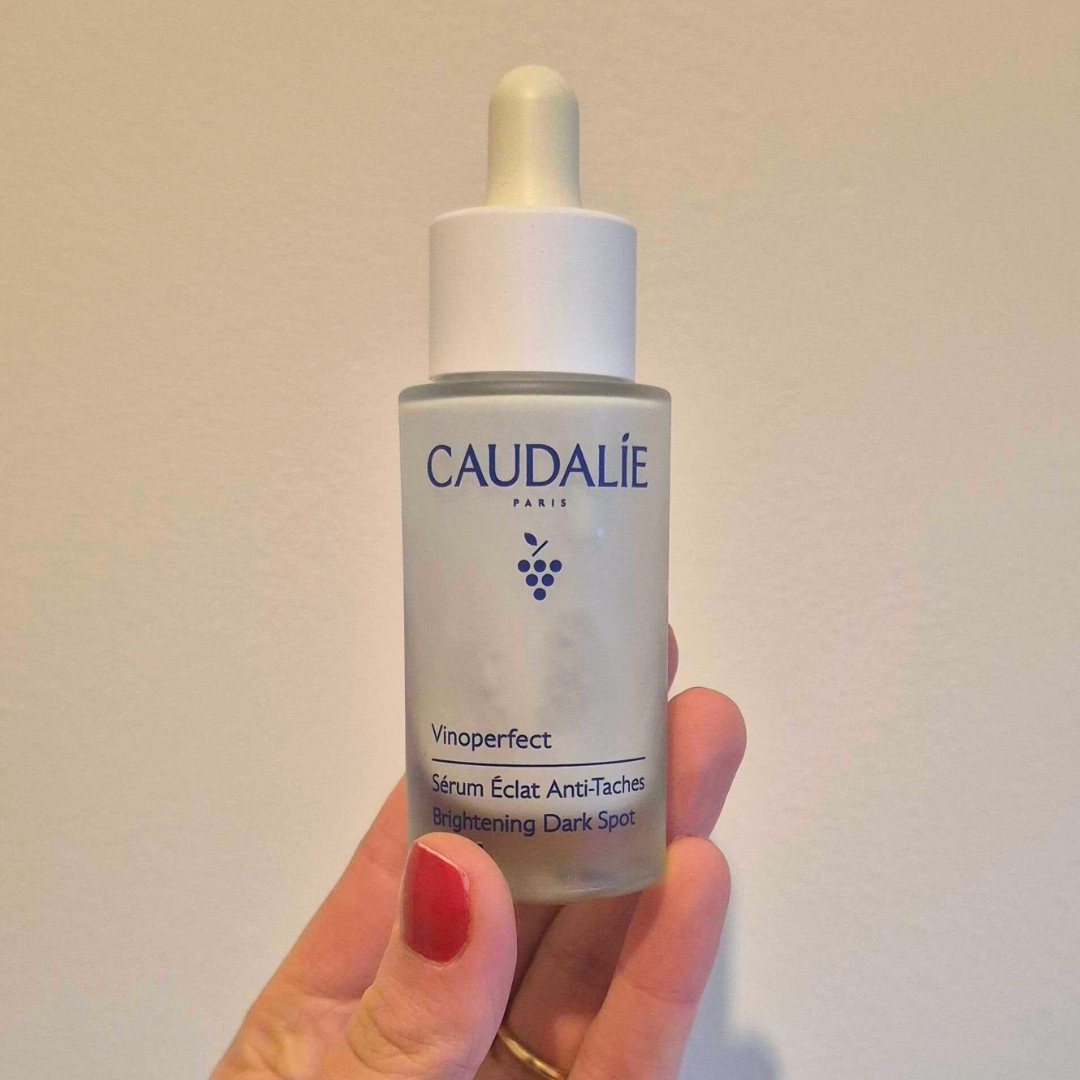 Hand holding empty white bottle of Caudalie Vinoperfect Brightening Dark Spot Serum