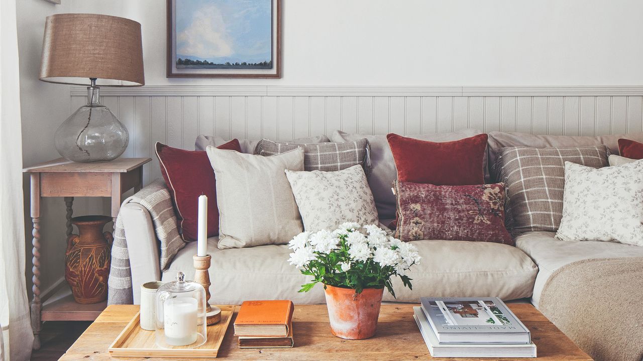 A living room with a beige corner sofa with multi-coloured scatter cushions and a vintage wooden coffee table and side table