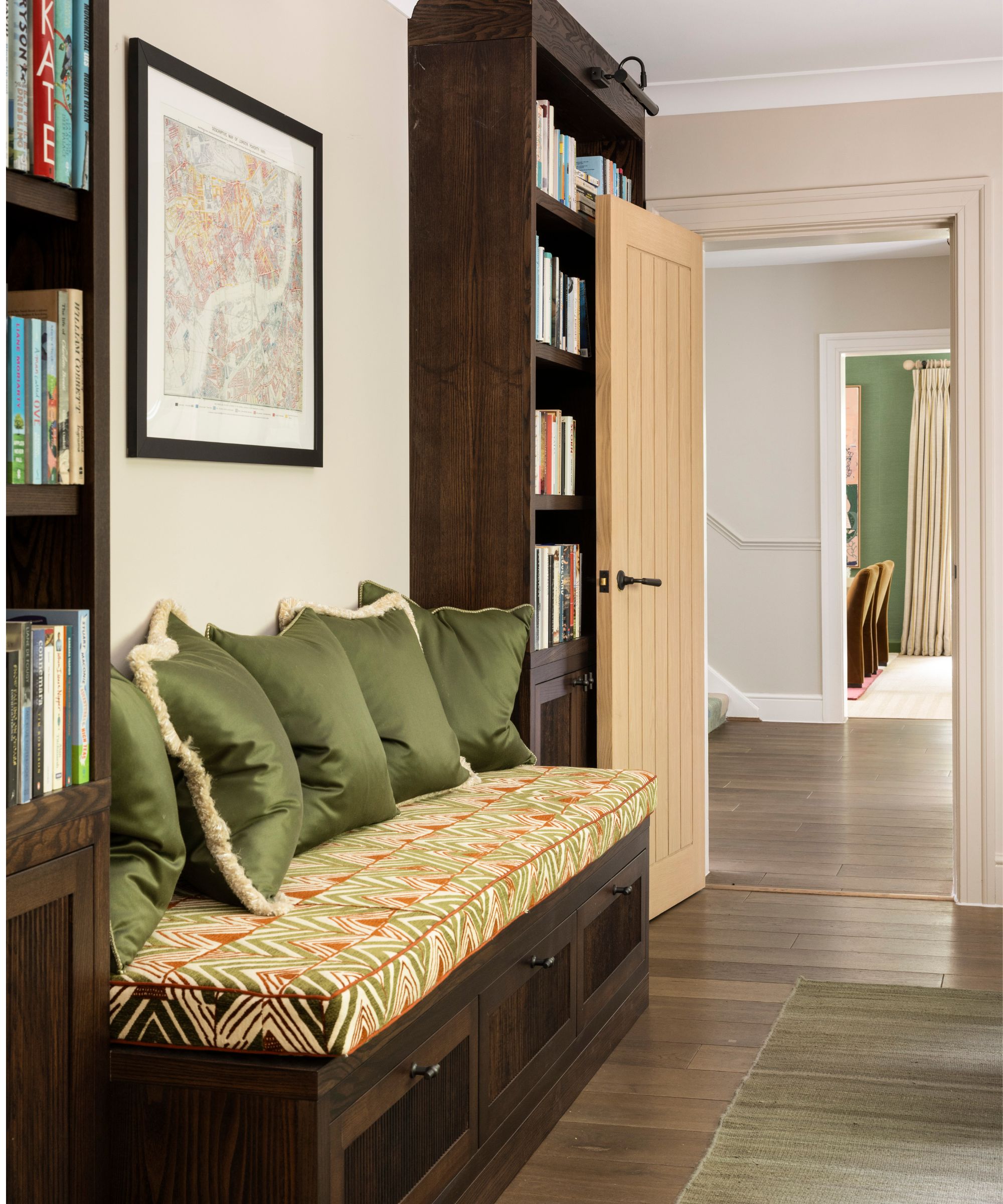a custom dark wooden bookcase and bench seat wall with green velvet cushions