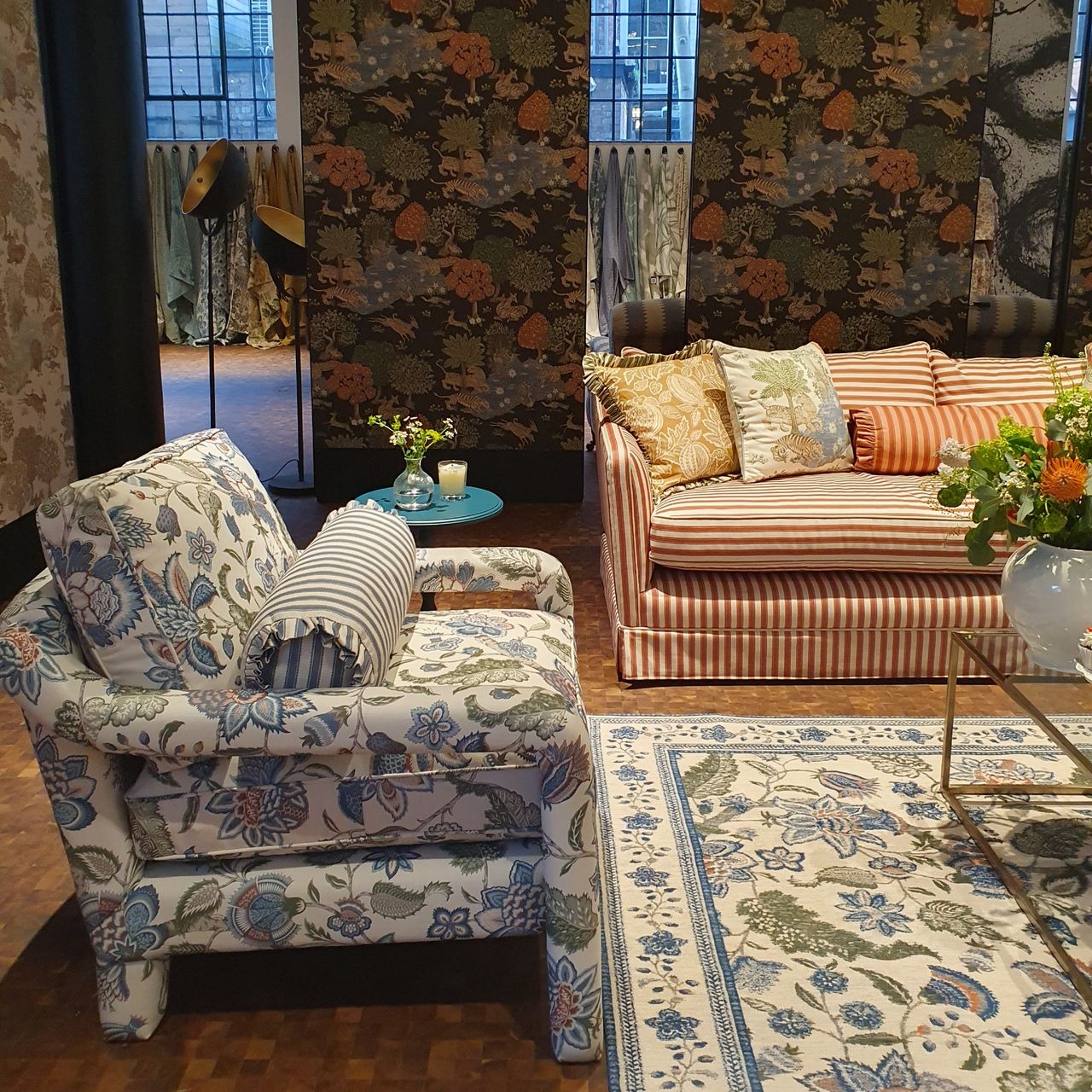 A living room with a striped sofa and a floral-print accent chair matching the floor rug