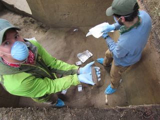 Researcher Aaron Costello (in the green jacket) holds the bone fragment of a large animal discovered during excavations