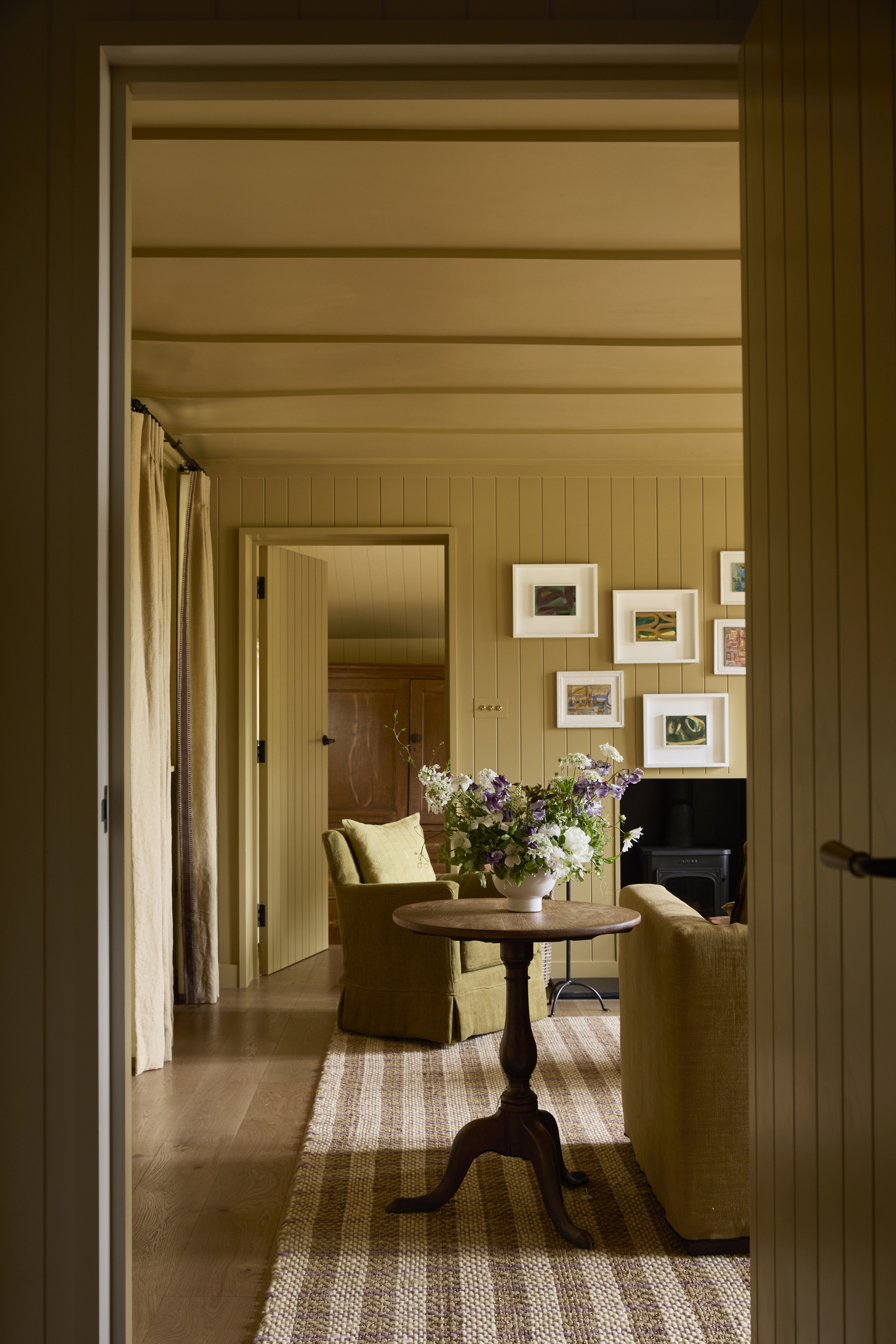 a living room painted in ochre yellow with a plaid rug, and a gallery wall