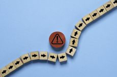 red circle block with red exclamation warning sign in the middle of a line of wooden blocks with black arrows