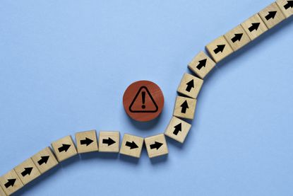 red circle block with red exclamation warning sign in the middle of a line of wooden blocks with black arrows