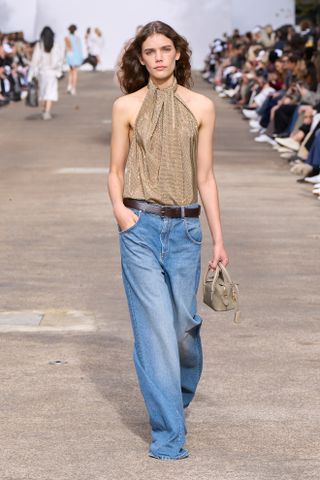 Model at the Stella Mccartney Spring 25 show in look 020 wearing a shimmery gold halter top and baggy jeans