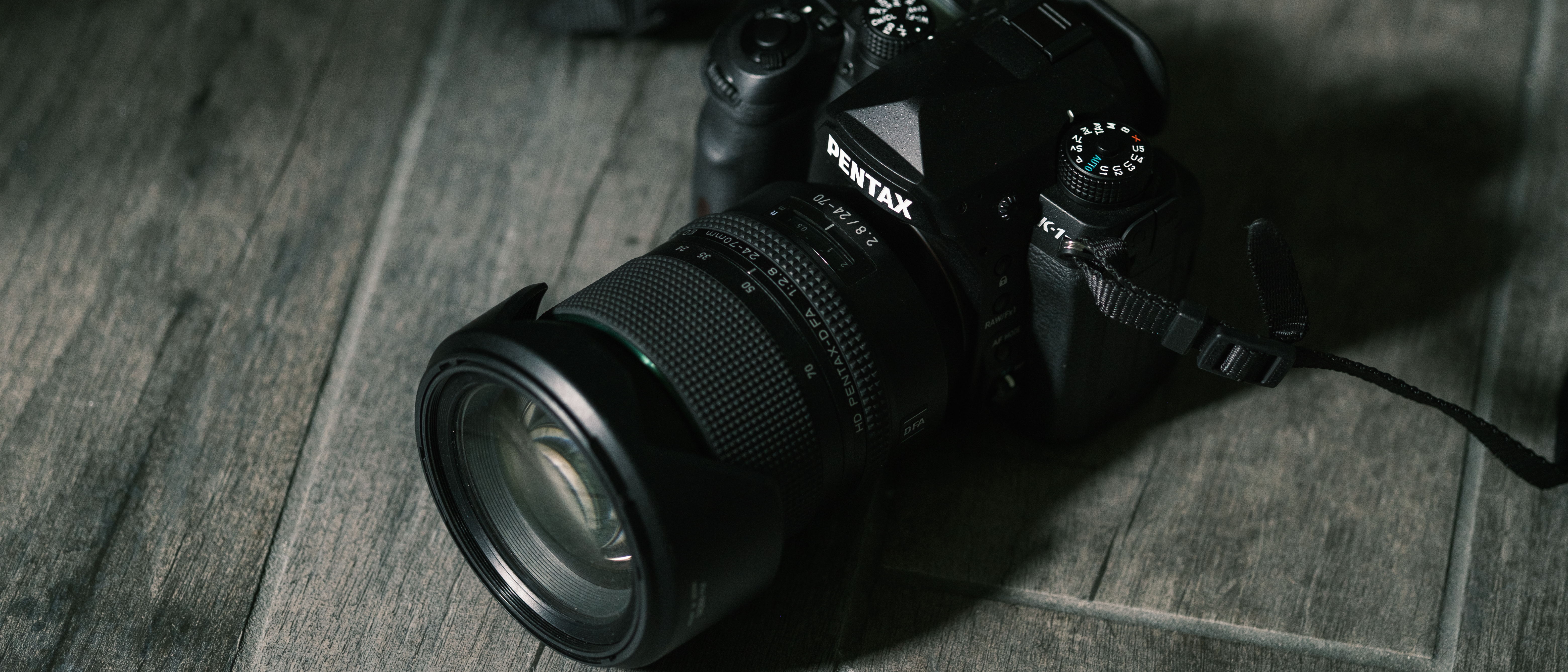 The Pentax 24-70mm f/2.8 on a gray wood texture background