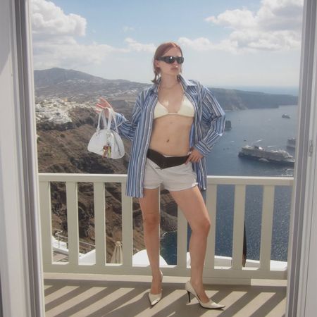 Lotta Lavanti wearing a striped button down over a bikini top and shorts holding a white bag. 