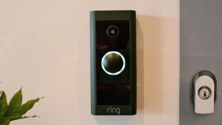 Ring Video Doorbell Wired installed by door, with a man and woman waving at the camera