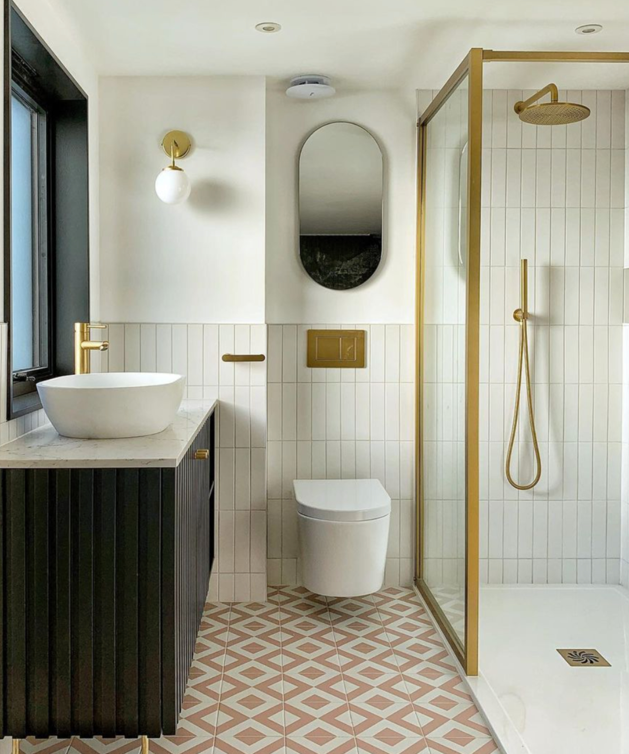 shower room with black vanity, wall hung toilet, gold and glass shower screen, pink floor tiles and white wall tiles