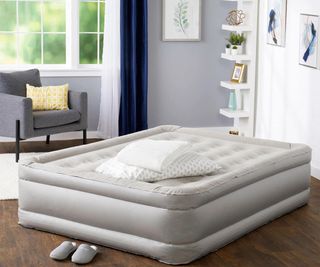 A pile of bedding on a gray air mattress against a blue living room wall.