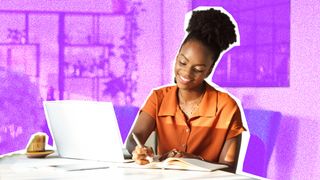 A woman sitting at a desk, writing in a notepad. A laptop is also on the table.