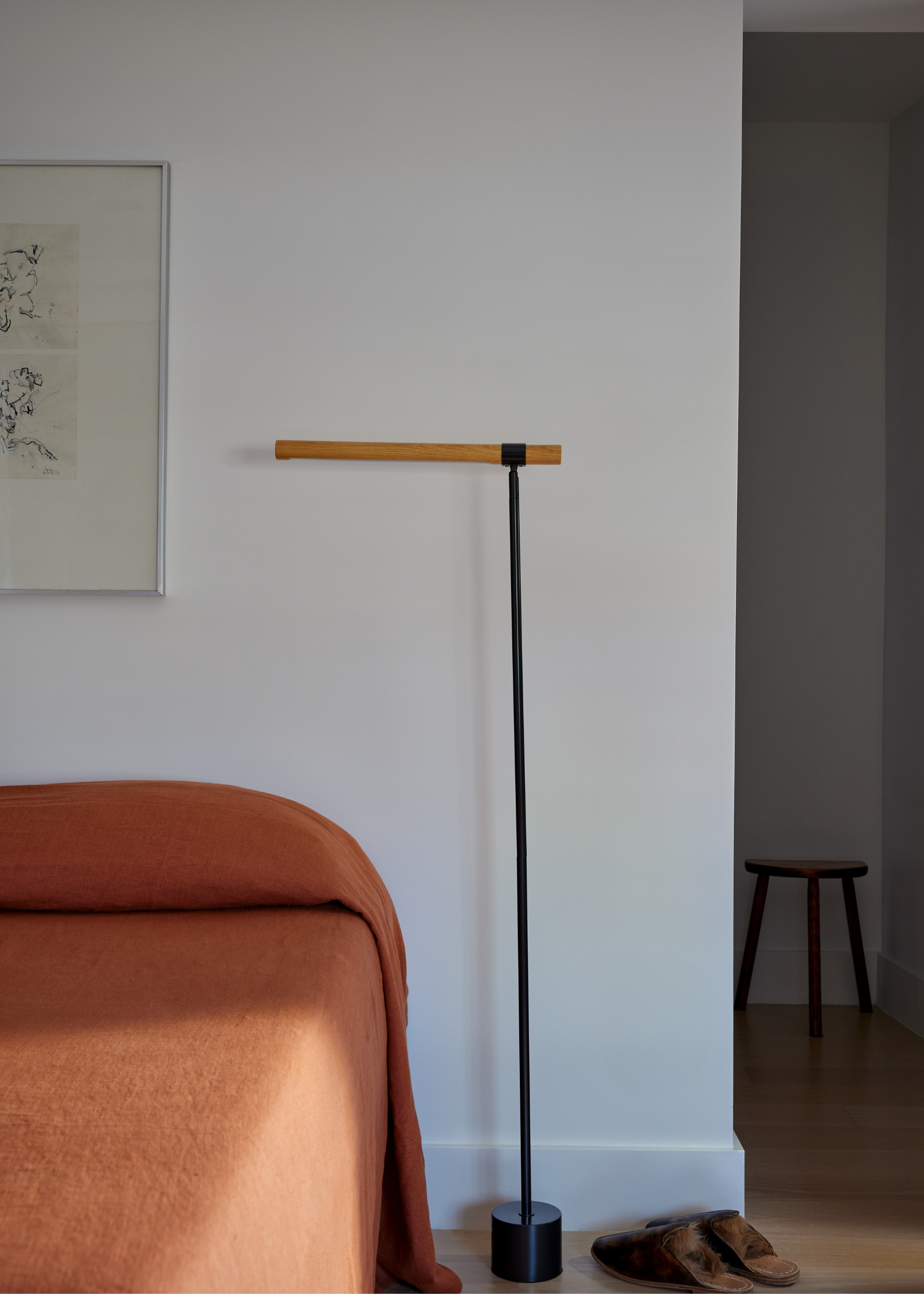 A white bedroom with a mustard bedscape, a standing floor lamp, and a framed painting on the wall