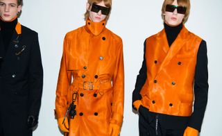 Three models in orange and black clothing against a white backdrop