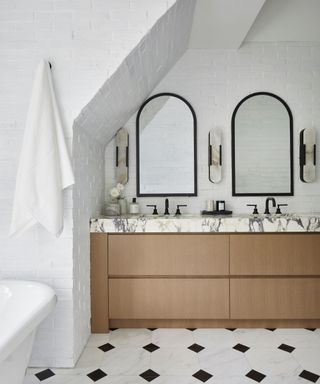 A bathroom with a double marble sink, two arched mirrors, and white brick walls