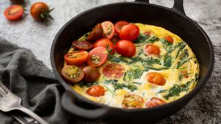 Omelet in cast iron frying pan with spinach and tomatoes, sitting on grey cloth