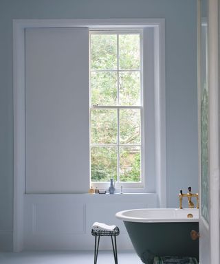 traditional bathroom with light blue walls, dark roll top bath, large window