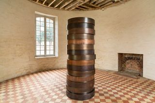 View of a piece made up of stacked metal discs by Sean Scully at Château de Boisgeloup. The space features distressed walls, a disused fireplace and checked flooring