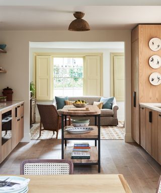 modern kitchen with lots of wood and a central freestanding island and a sofa in the background with pale yellow window shutters