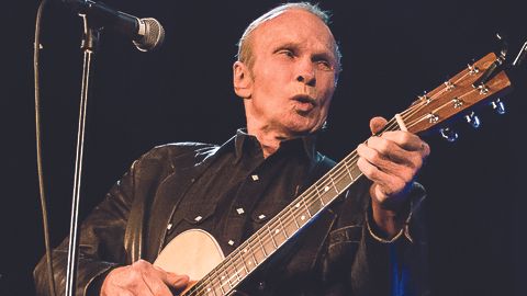 Phil Alvin playing electric guitar and pursing his lips near the microphone.