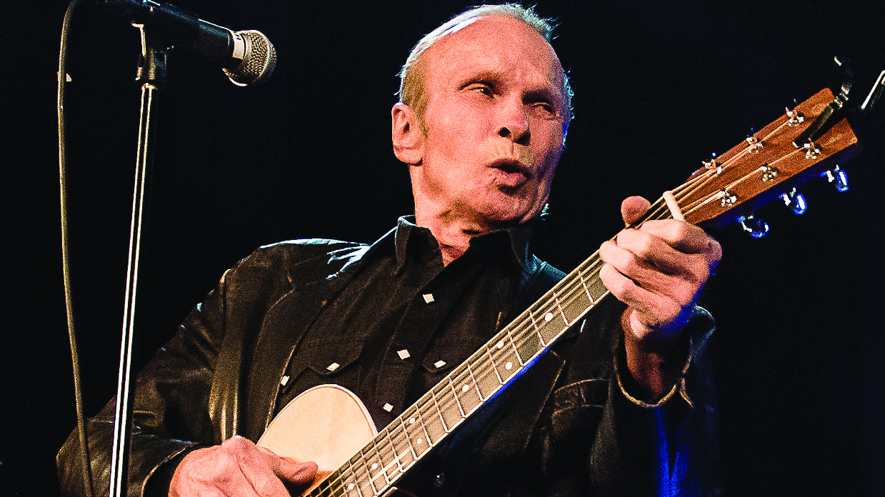 Phil Alvin playing electric guitar and pursing his lips near the microphone.