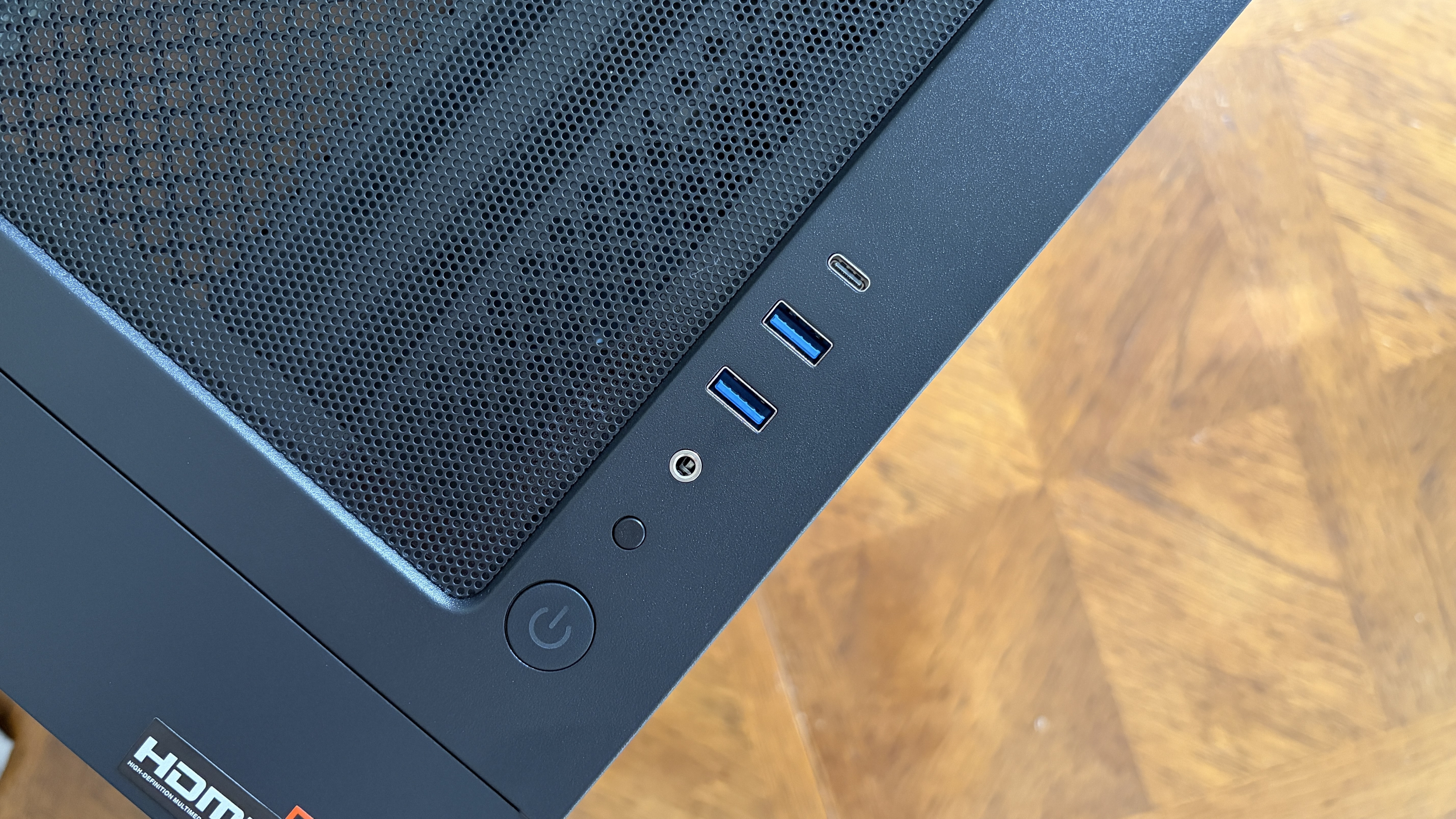 Top view of a black Nitro 65 computer case showing USB ports, a power button, and a ventilation grill, placed on a wooden surface.