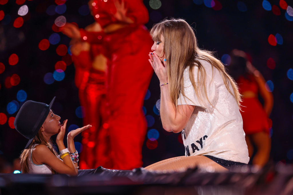 A young fan exchanges friendship bracelets with Taylor Swift as she performs onstage during "Taylor Swift | The Eras Tour