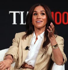 Meghan Markle wearing a tan suit sitting in a chair talking