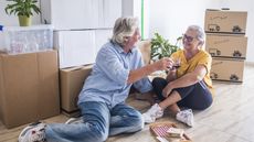 An older couple sitting on the floor with boxes around them, having just moved into their new home.