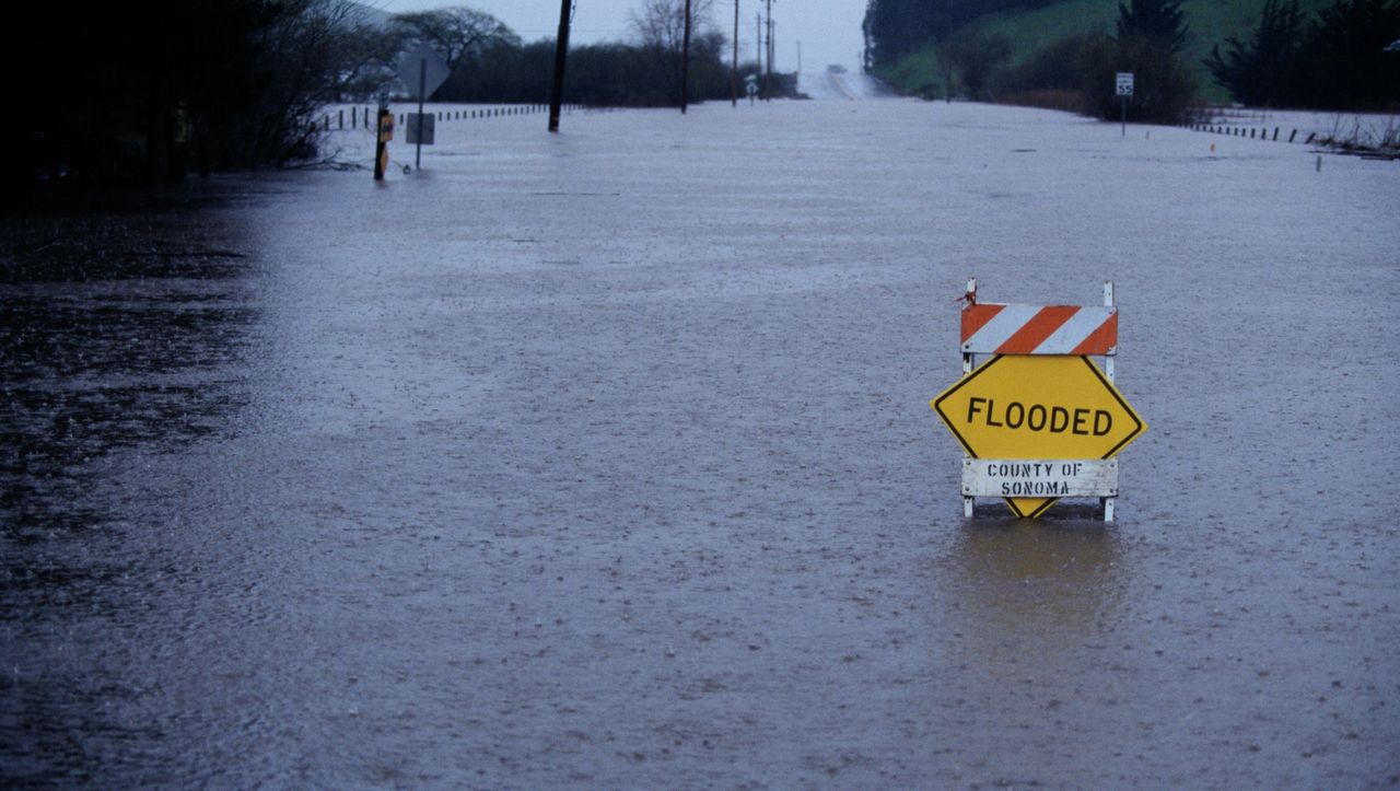 A warning sign saying &quot;flooded&quot; in the middle of a flooded street in the rain.