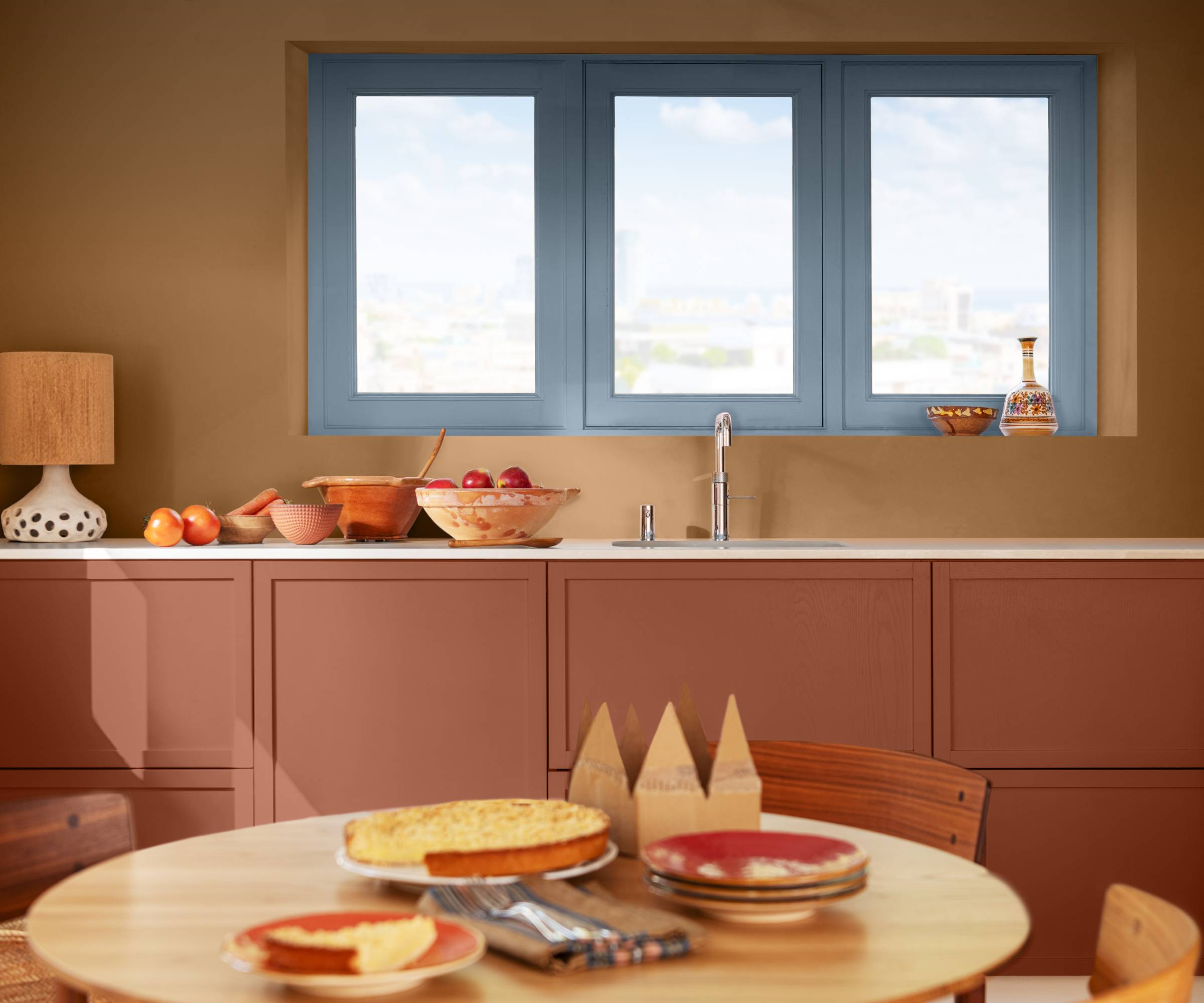 kitchen with walls and units painted in shades of terracotta and window frame in blue