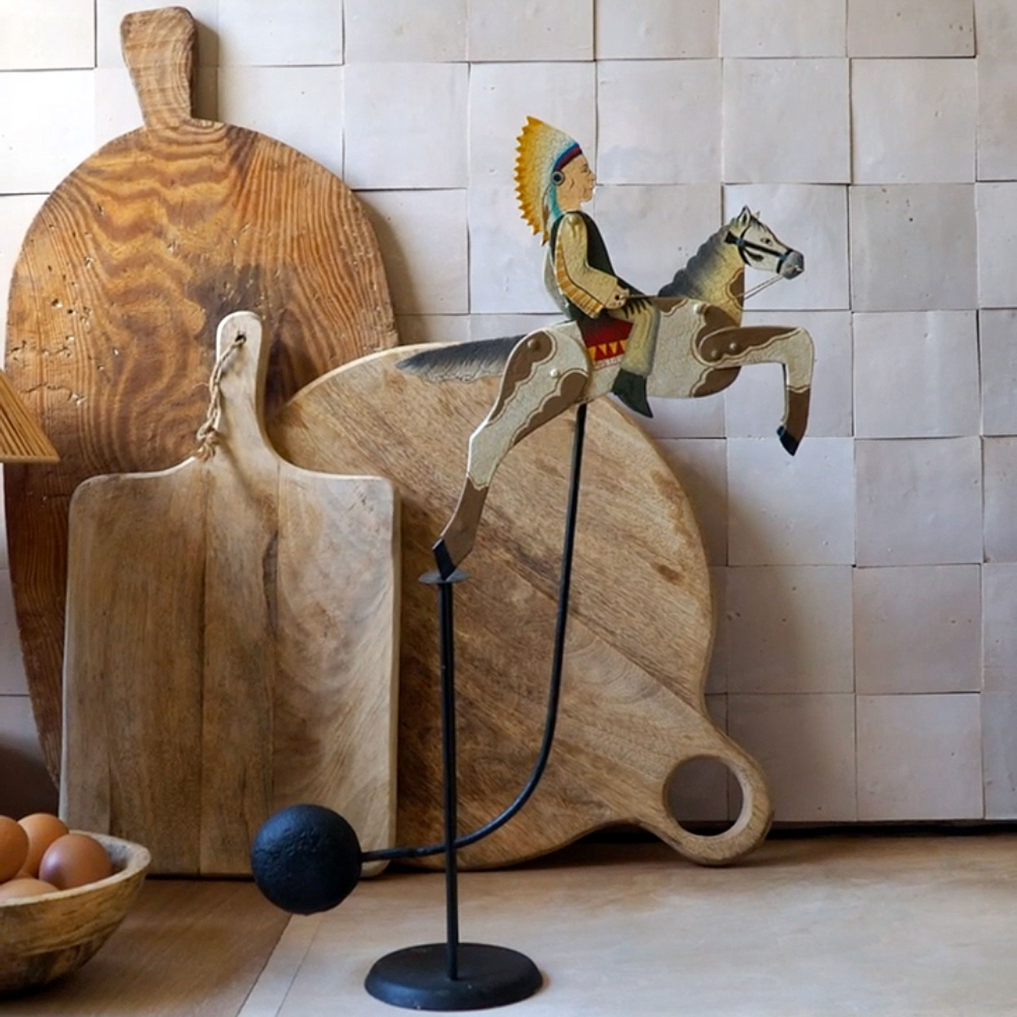 Pendulum cowboy toy in front of three wooden chopping boards