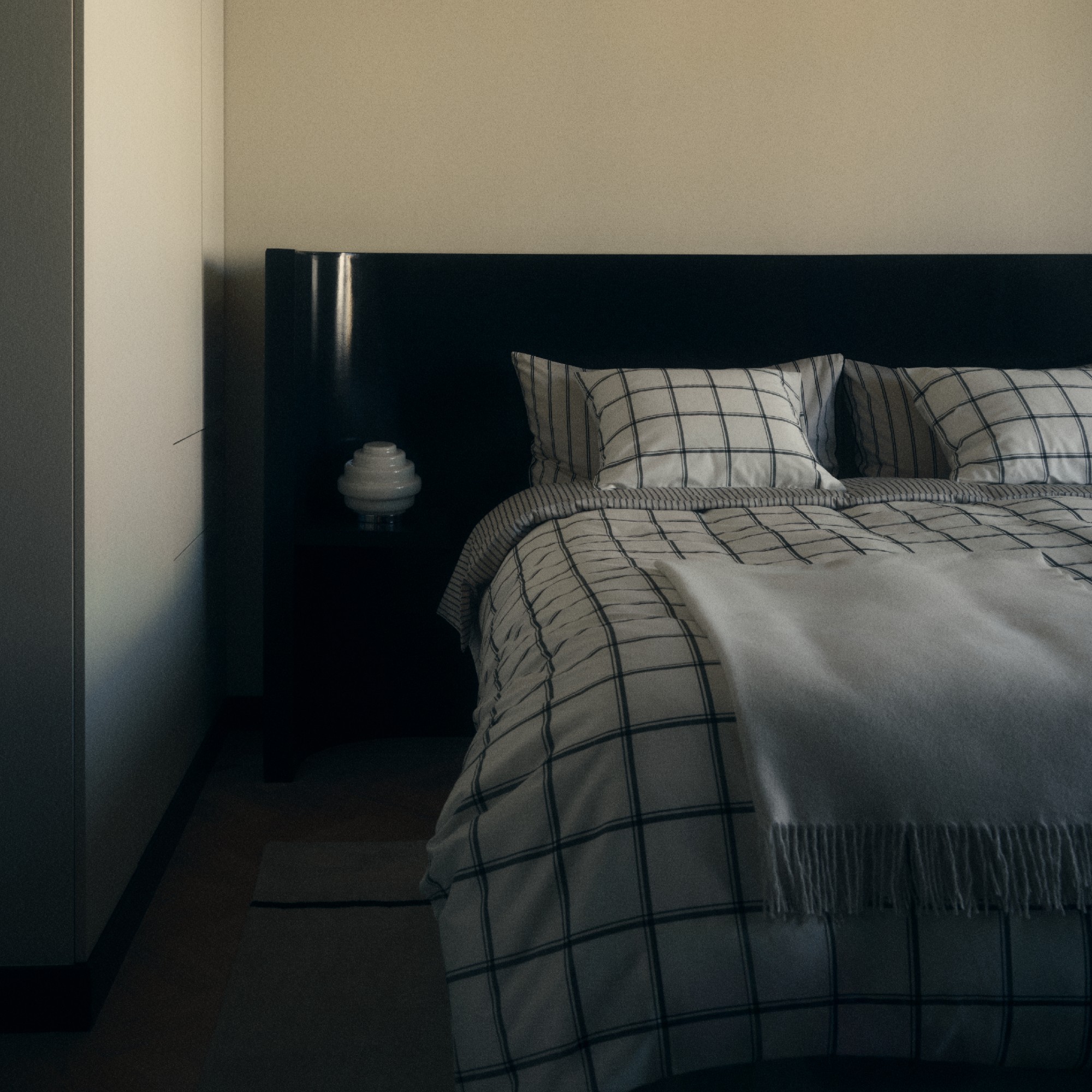 A monochrome bedroom with a curved black glossy headboard and checked black and white bedding