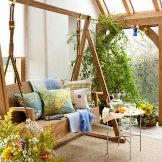White conservatory with wooden and wicker sofa swing with floral cushions