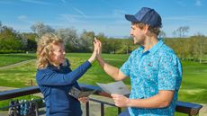 two golfers high-five with smiles on their faces while holding scorecards