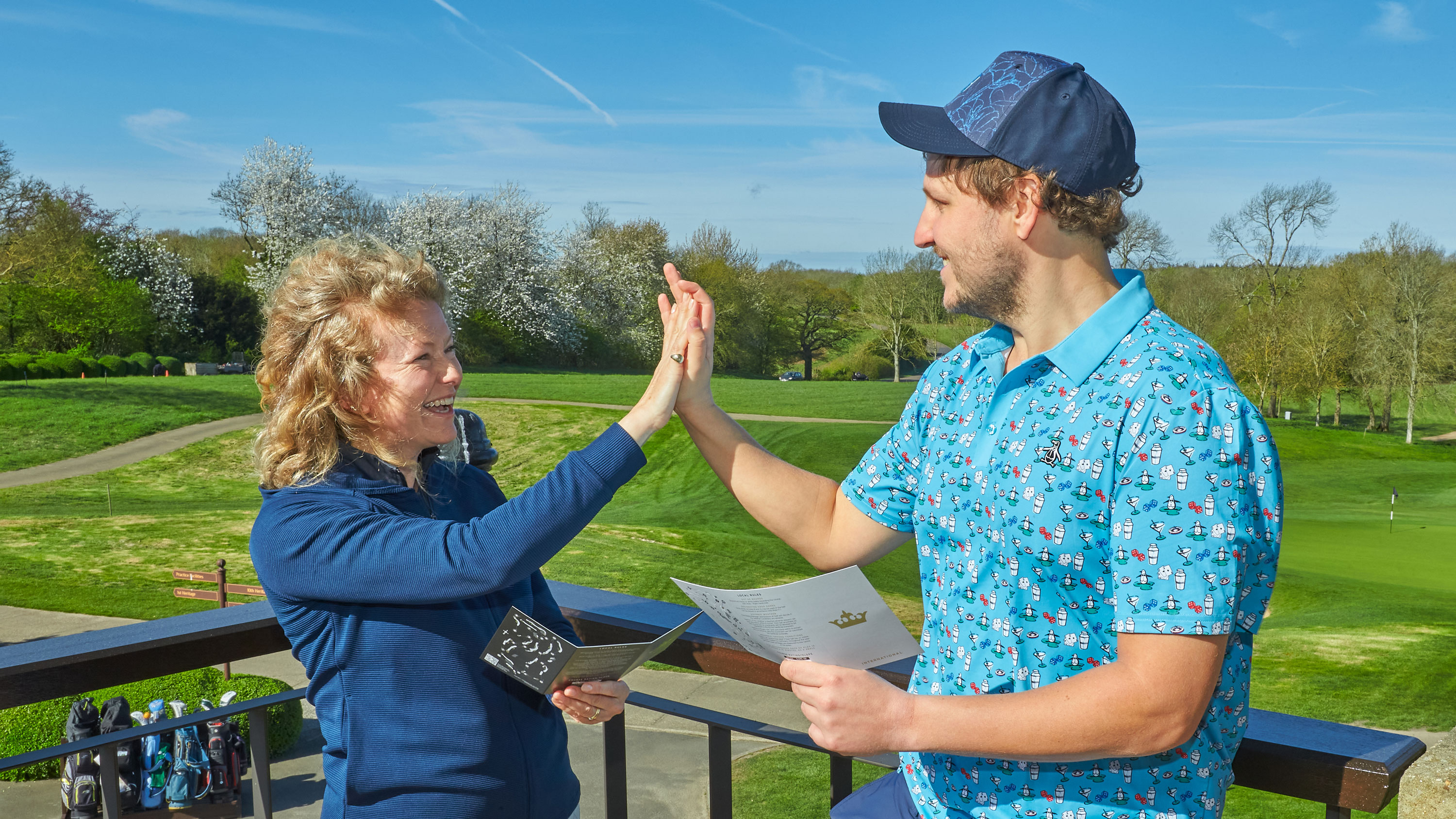 two golfers high-five with smiles on their faces while holding scorecards