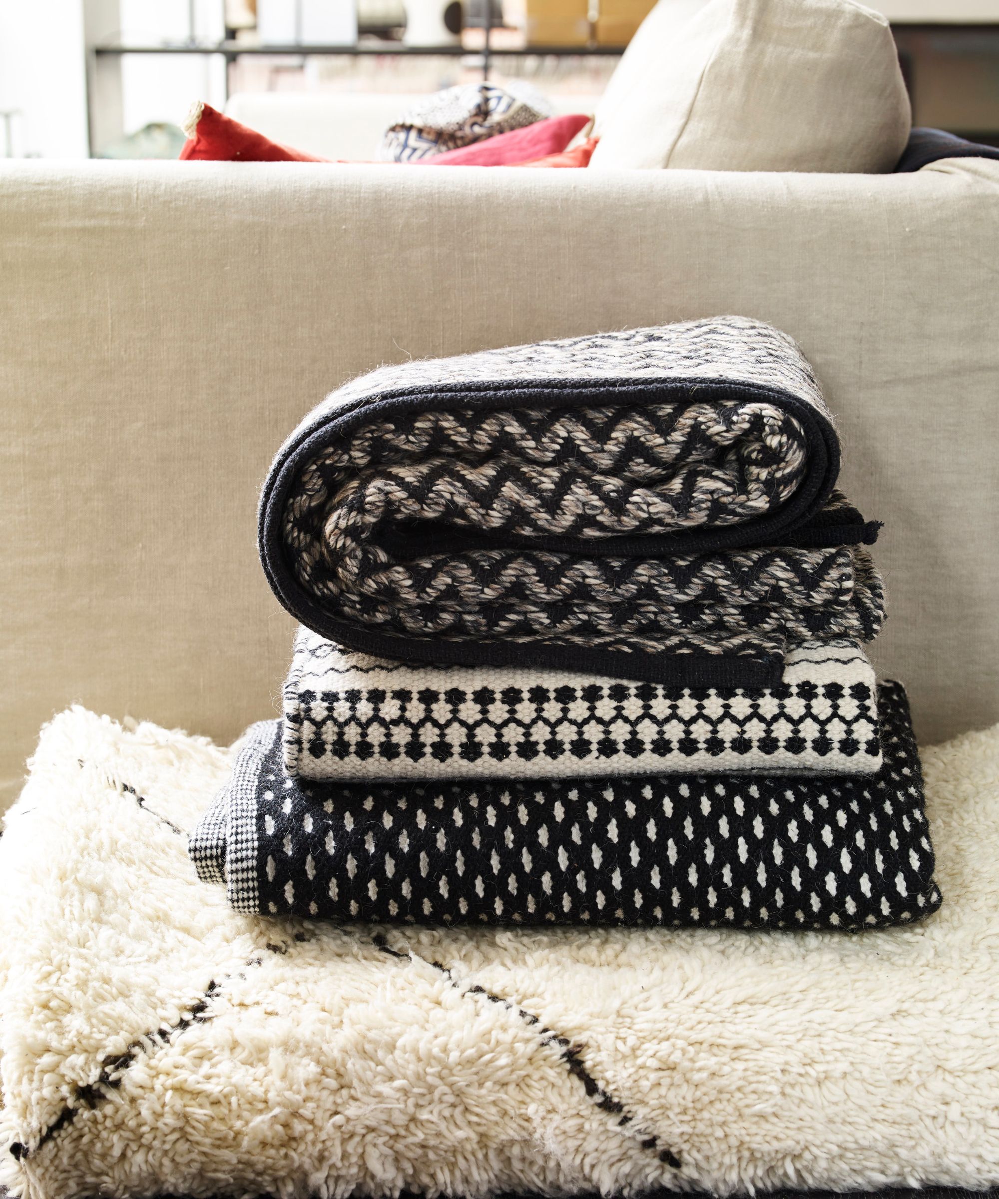 Stack of black and white patterned throw blankets in front of a cream sofa
