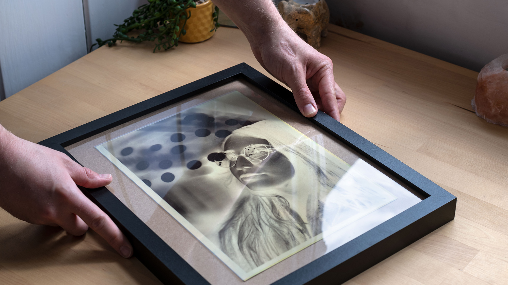Hands placing a picture frame over a negative of a portrait, placed in window light to expose the image