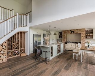 A modern farmhouse style country kitchen with wine rack under the stairs, wooden flooring and grey island