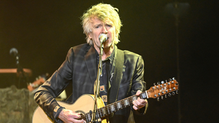 Neil Finn playing an acoustic guitar on stage