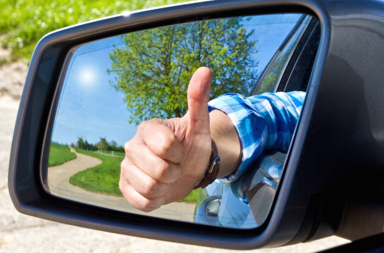 Car driver ith thumb up in a side mirror