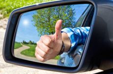 Car driver ith thumb up in a side mirror