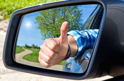 Car driver ith thumb up in a side mirror