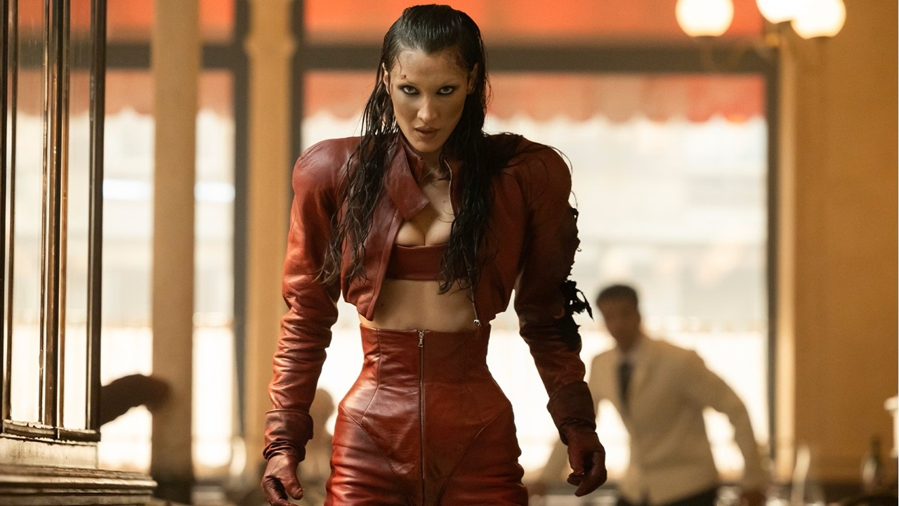 A intense-looking supermodel (Bella Hadid) wearing a burgundy jacket and high-waisted trousers looks poised to attack inside a restaurant dining room in The Beauty.
