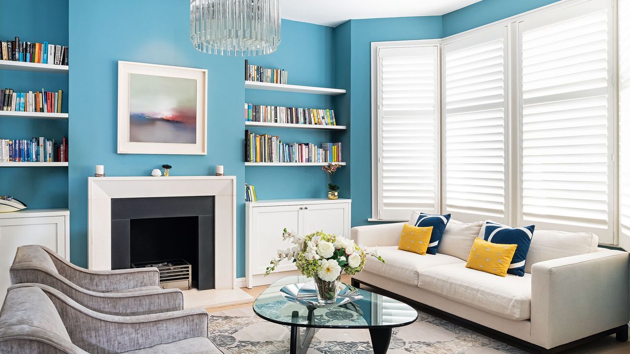 Blue living room with bookshelves, fireplace, chandelier and grey sofa in front of mirror