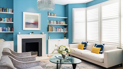 Blue living room with bookshelves, fireplace, chandelier and cream sofa in front of mirror